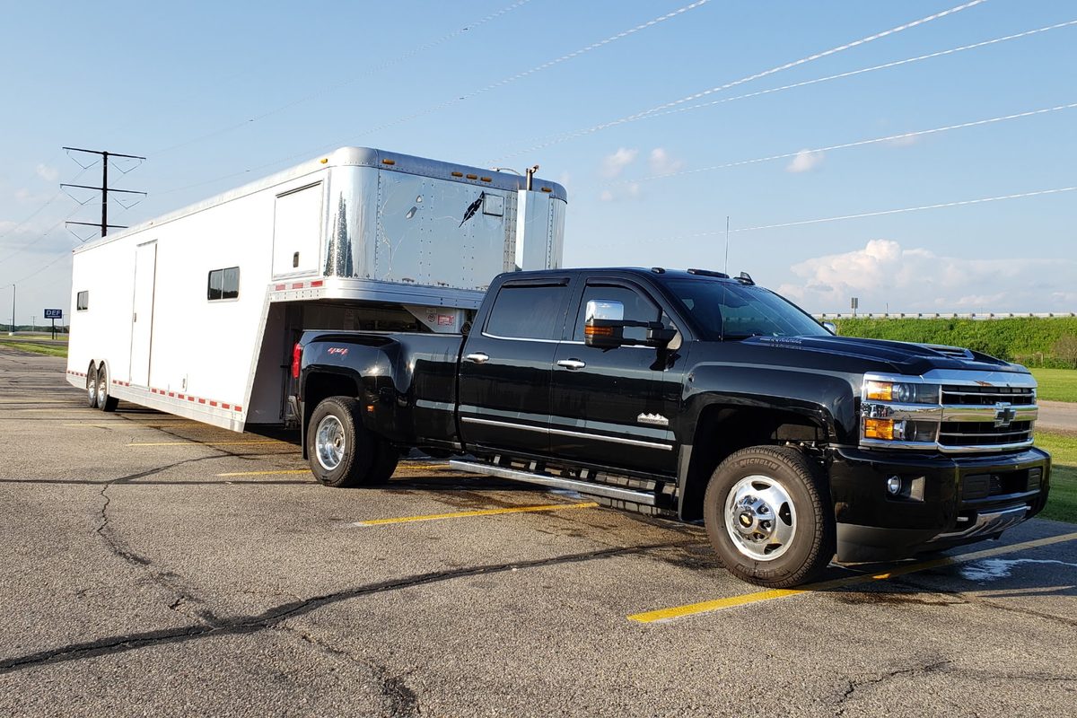 Black one-ton dually pickup towing a white enclosed gooseneck trailer with an aluminum nose