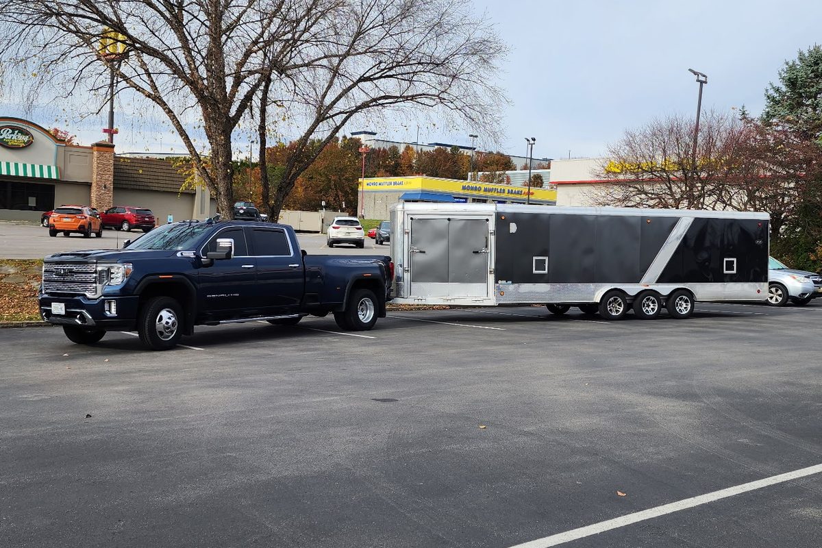 Blue GMC Sierra 3500HD Denali dually towing a black and silver triple-axle enclosed trailer