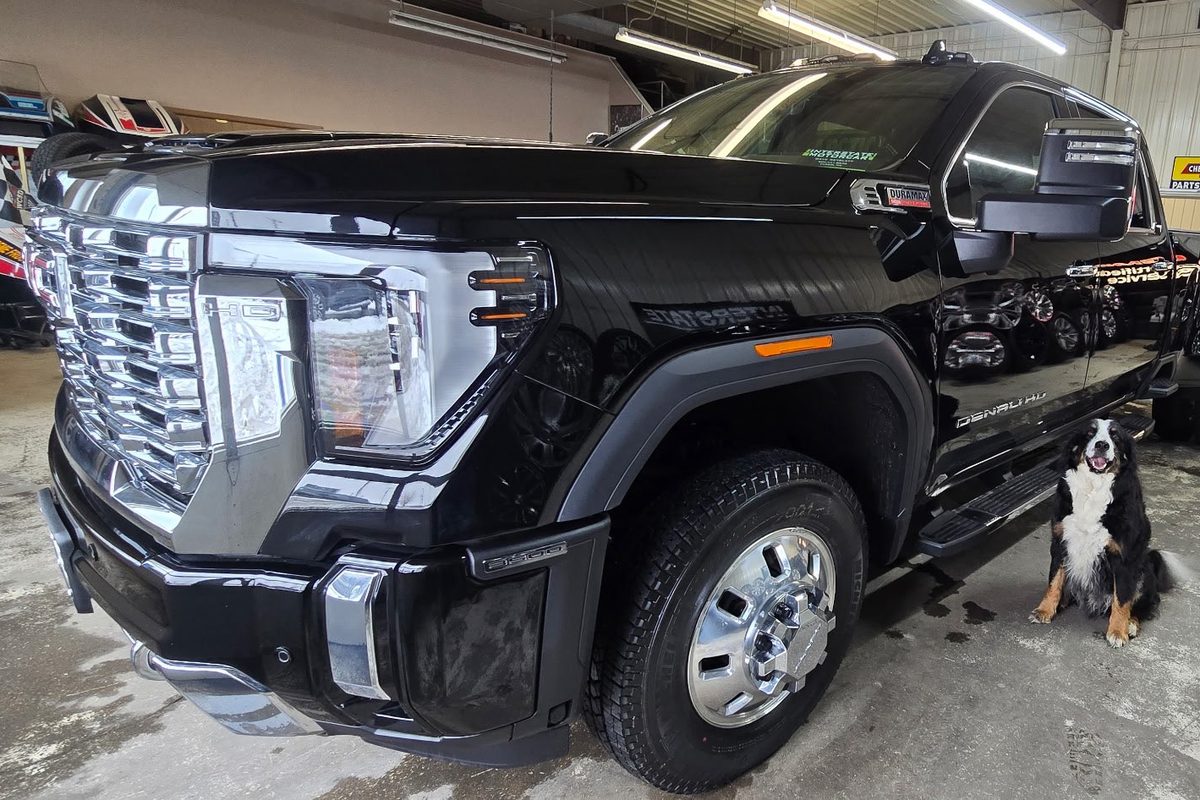 Black current-generation GMC Sierra 3500HD Denali dually in a service shop, with a dog sitting beside it