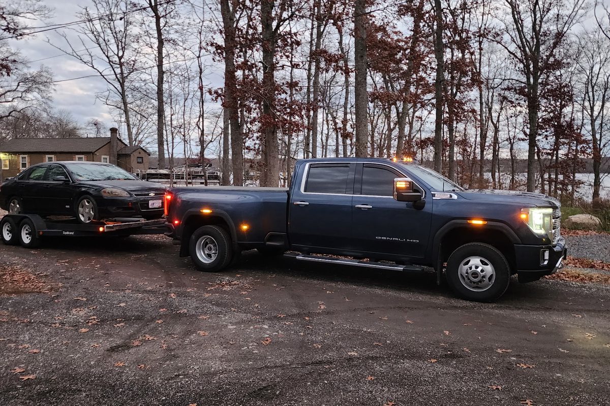 Blue GMC Sierra 3500HD Denali dually towing an open tandem-axle car trailer loaded with a black Chevrolet Impala