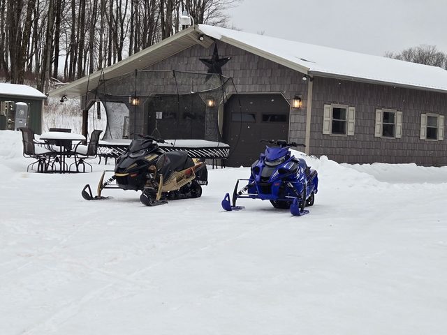 Two Yamaha sleds parked in fresh snow outside the garage
